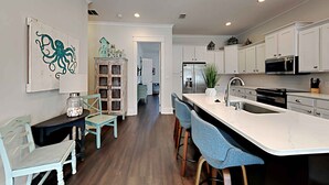 A modern kitchen with white cabinets, a central island with bar stools, and a dining area with a table and chairs. - Casa Migos by Southern Vacation Rentals (Panama City Beach)