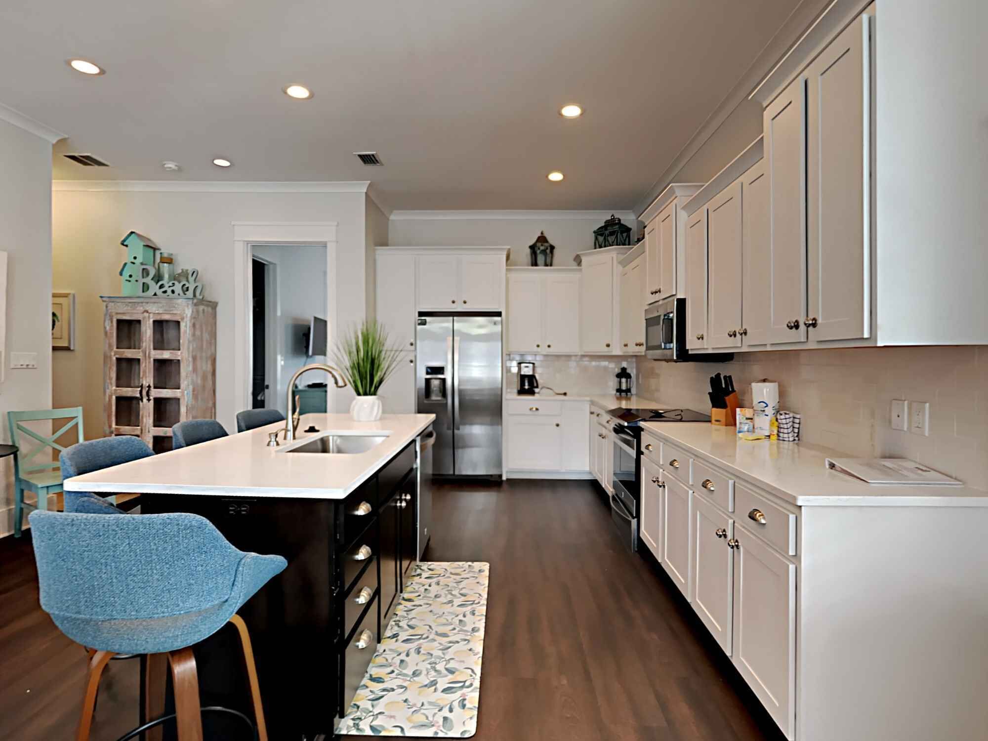 A modern kitchen with white cabinetry, a central island, and a dining area with blue chairs.