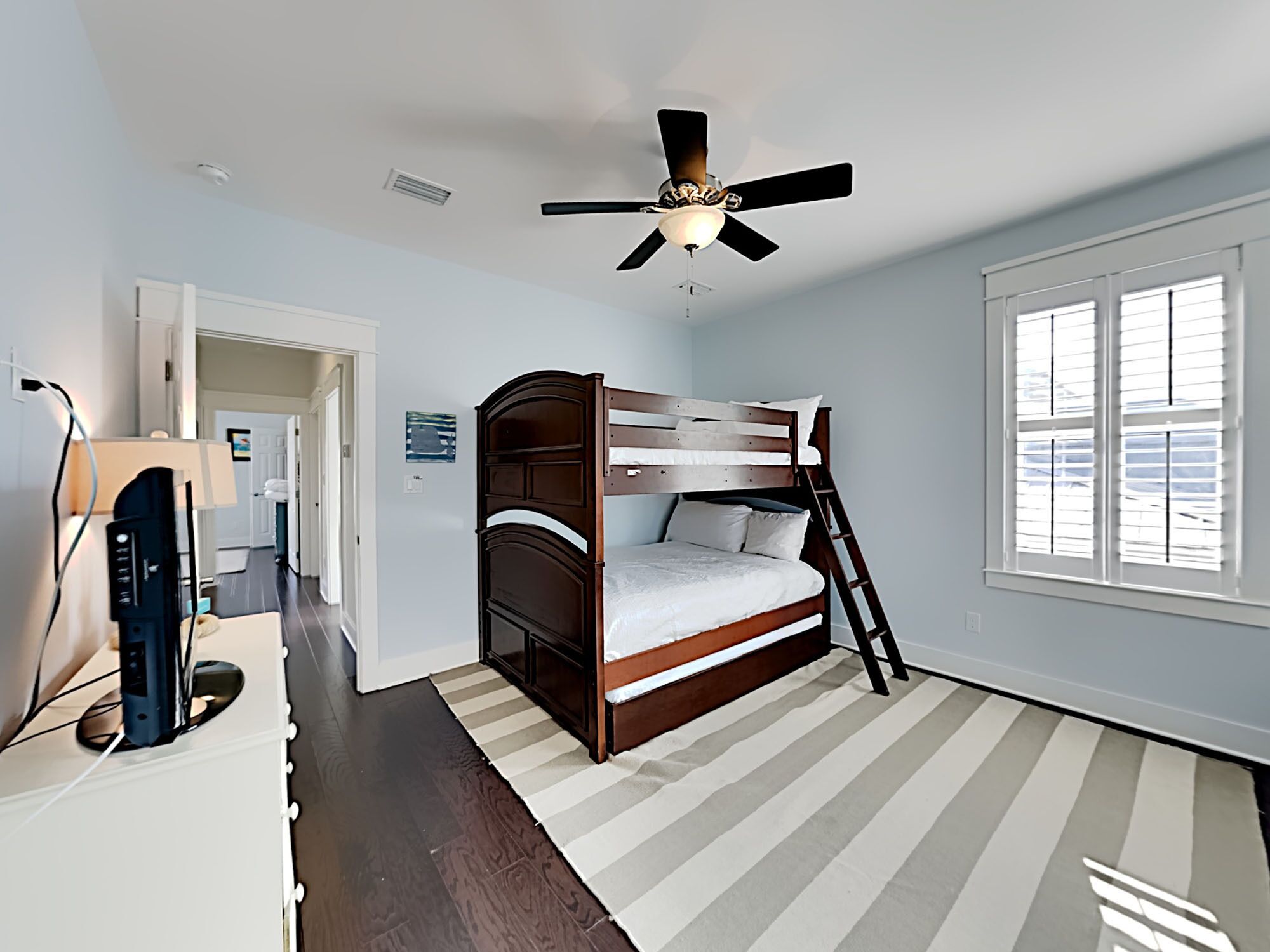 A bedroom with a bunk bed, a ceiling fan, a window with blinds, and a striped rug.