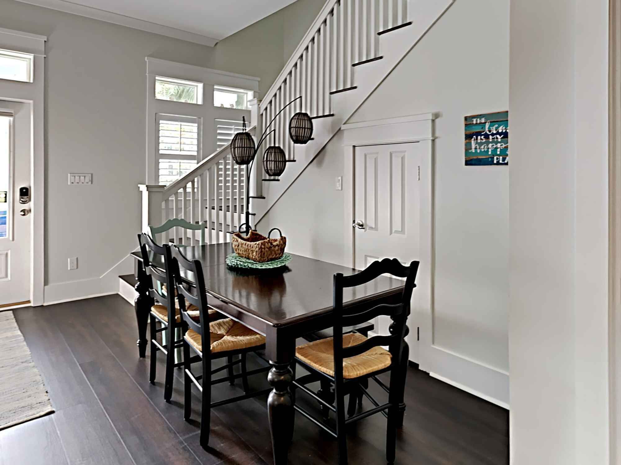 A dining area with a dark wooden table, six chairs, a woven basket, and a staircase with black lanterns.