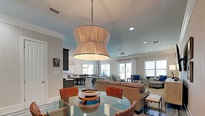 A spacious living room with a glass-top dining table surrounded by wicker chairs, a large sofa, and a coffee table with decorative items. - Beach Music by Southern Vacation Rentals (Orange Beach)