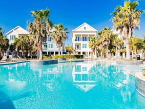 Een resort met een groot zwembad, palmbomen en meerlaags gebouwen.