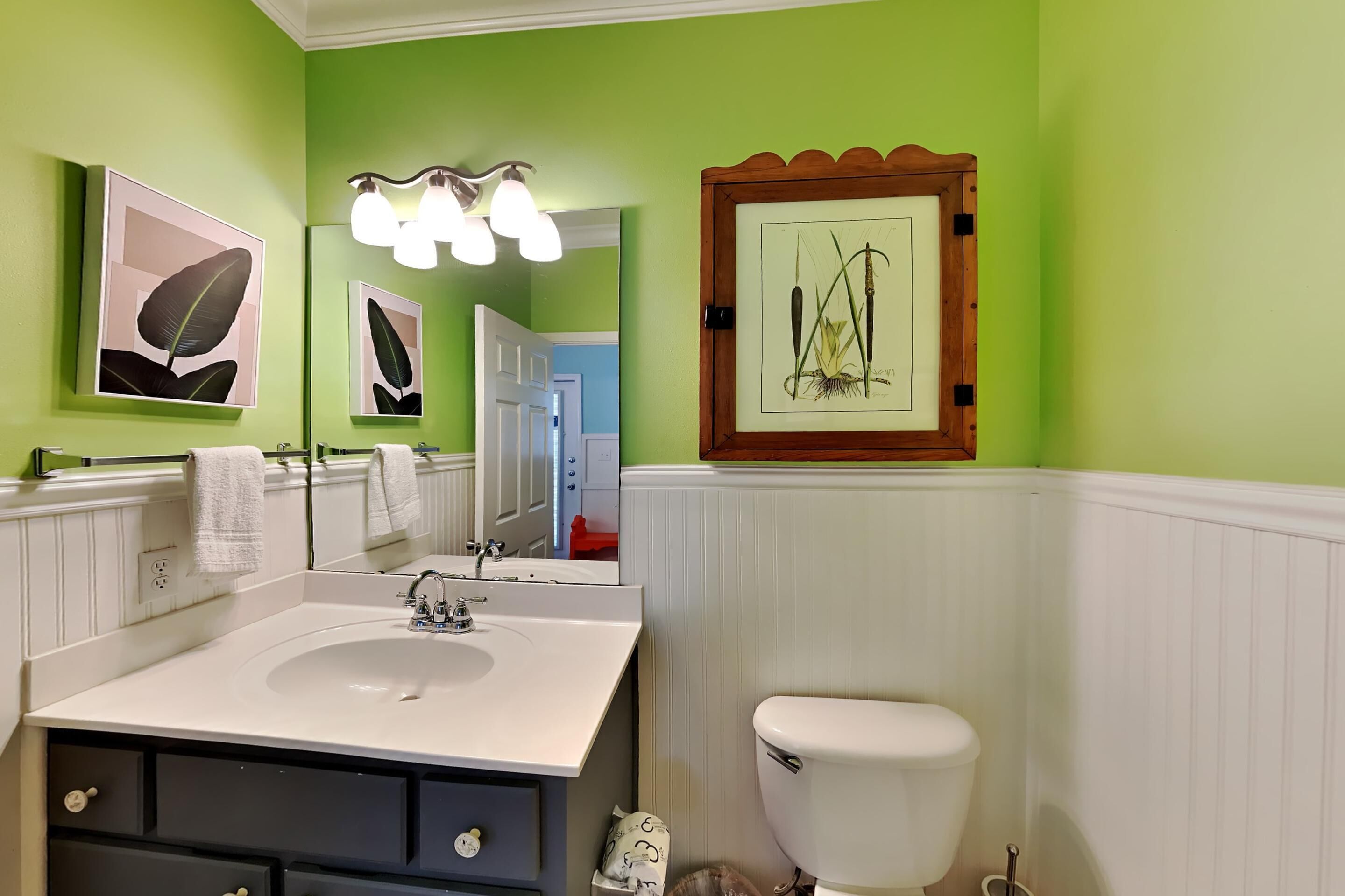 A bathroom with a white sink, dark cabinets, a white toilet, and green walls.