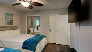 Une chambre d’hôtel avec un lit, un ventilateur de plafond, une télévision et une porte.