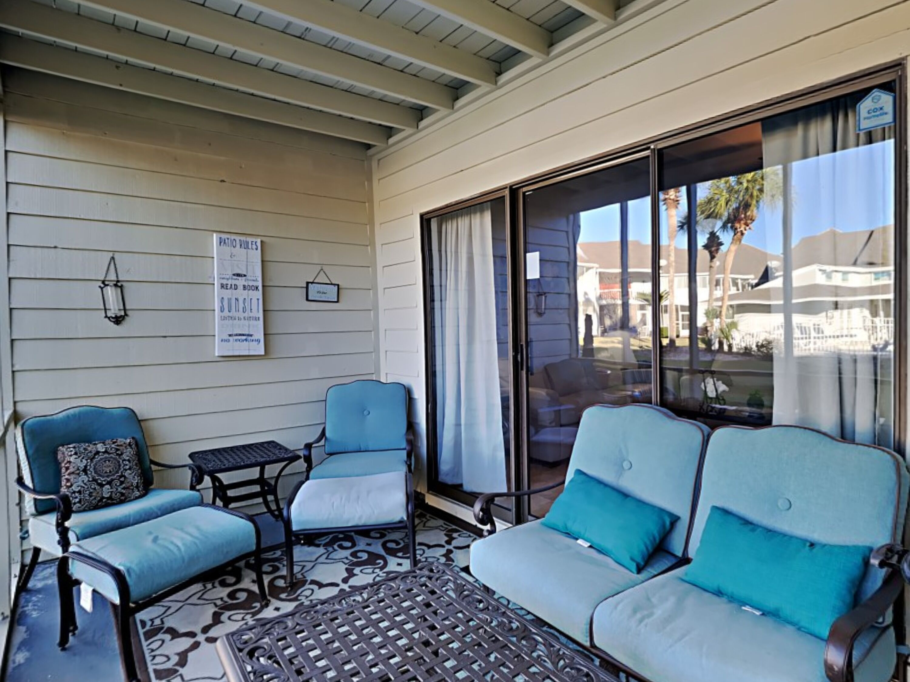Un patio couvert avec deux fauteuils bleus dotés de coussins, une petite table et un tapis à motifs.