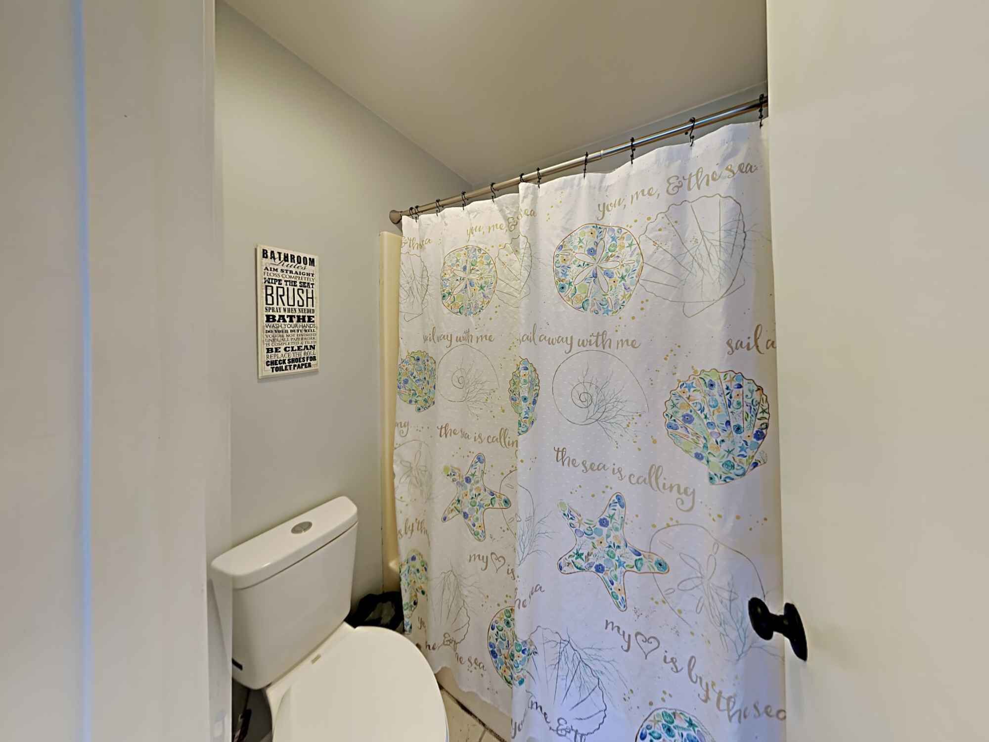 Un baño con inodoro, cortina de ducha con motivos florales y un cartel con indicaciones.
