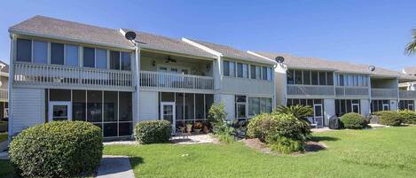 A row of two-story apartment buildings with balconies, a grassy lawn, and a pathway leading to the entrance.