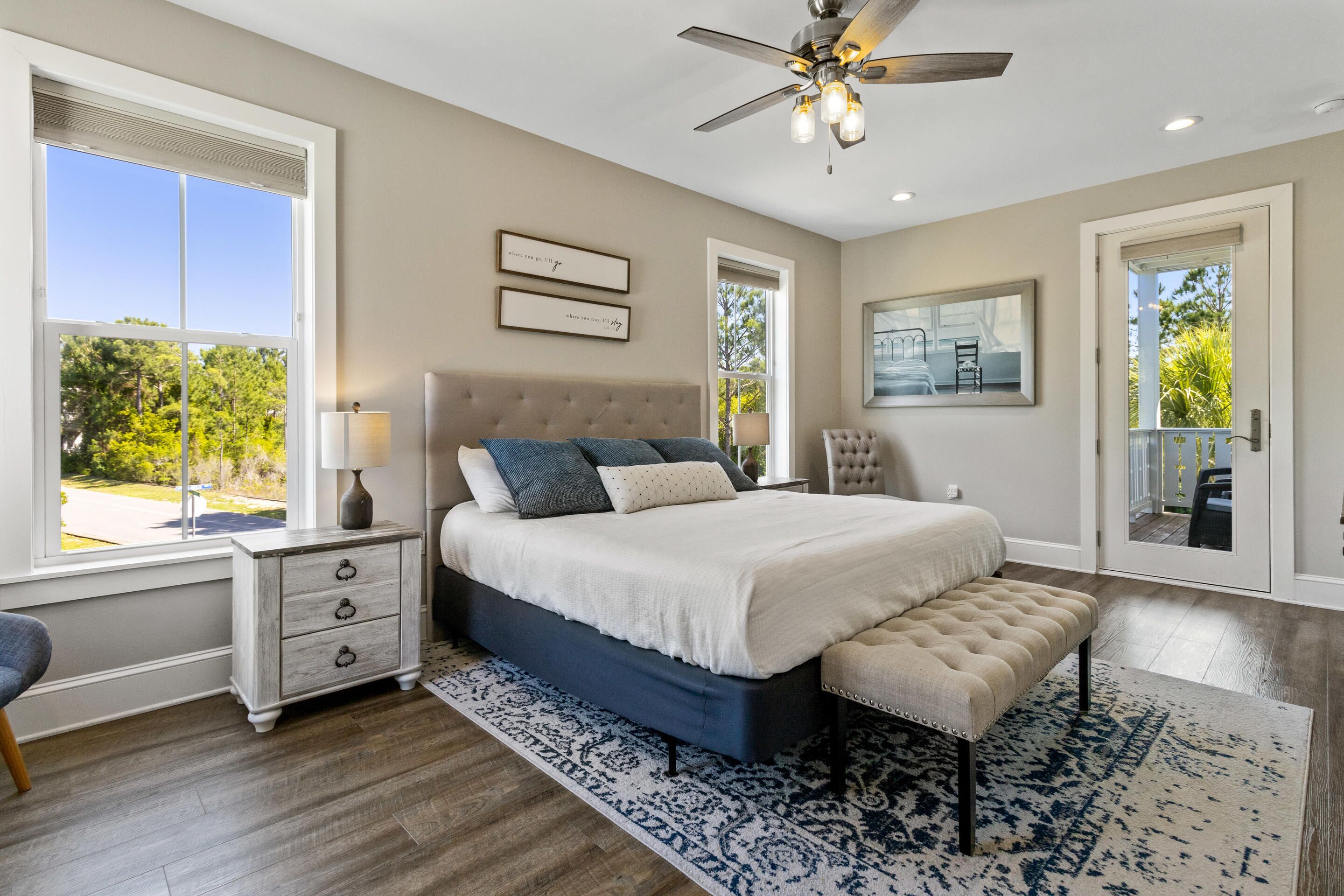 A bedroom with a large bed, a ceiling fan, and a view of the outdoors.