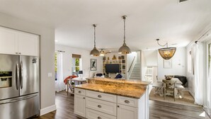 A modern kitchen with a central island, stainless steel appliances, pendant lighting, and a dining area with a staircase leading to an upper level. - Easy Breezy by Southern Vacation Rentals (Santa Rosa Beach)