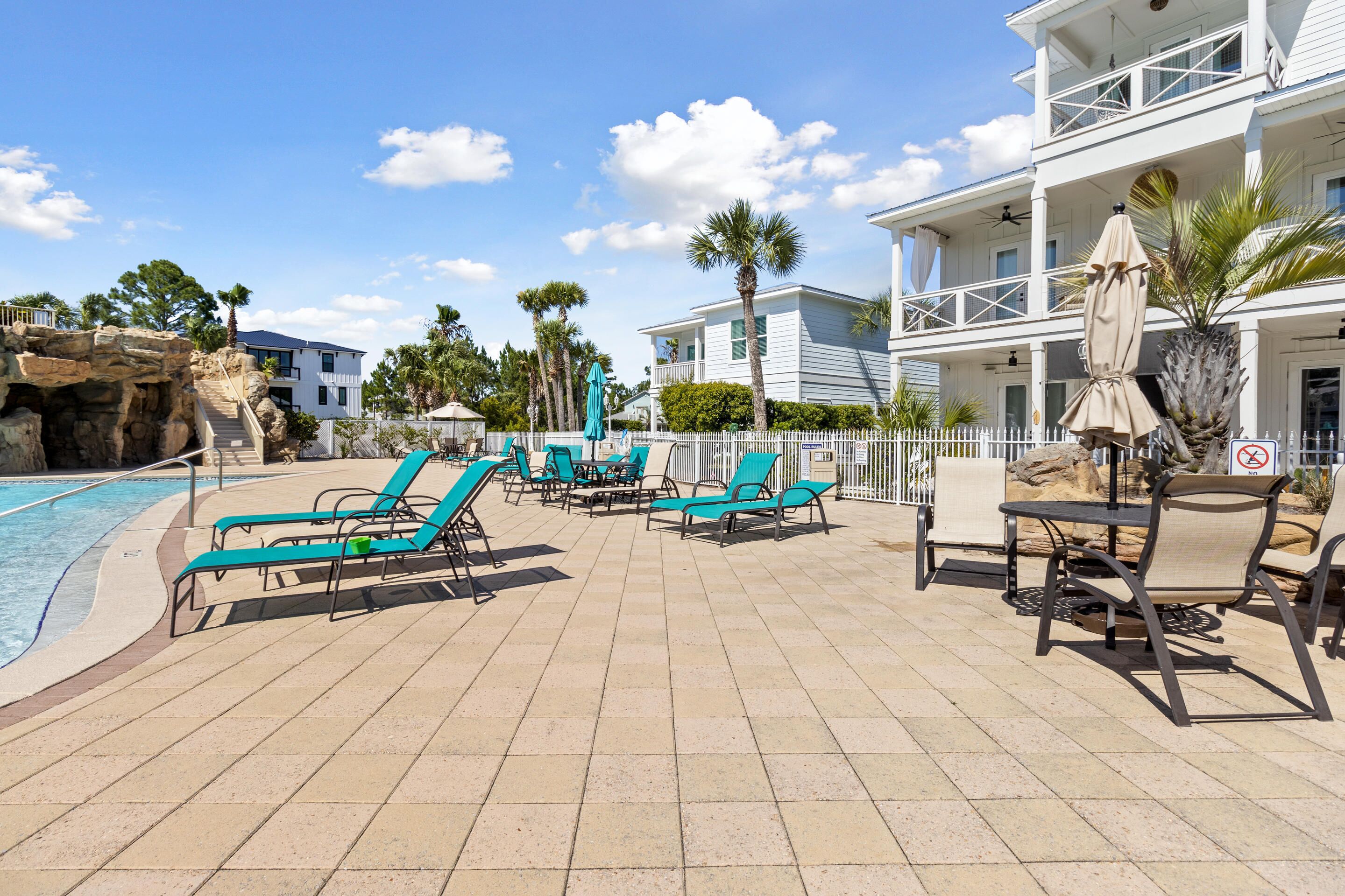 A poolside area with lounge chairs and umbrellas, a pool, and a building with balconies.