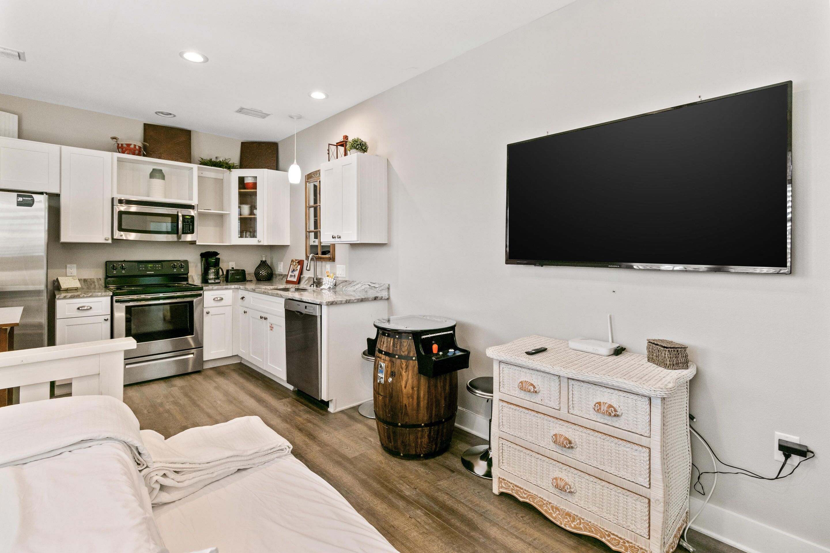 Une cuisine moderne avec des meubles blancs, un grand téléviseur à écran plat fixé au mur et un tonneau en bois utilisé comme élément décoratif.