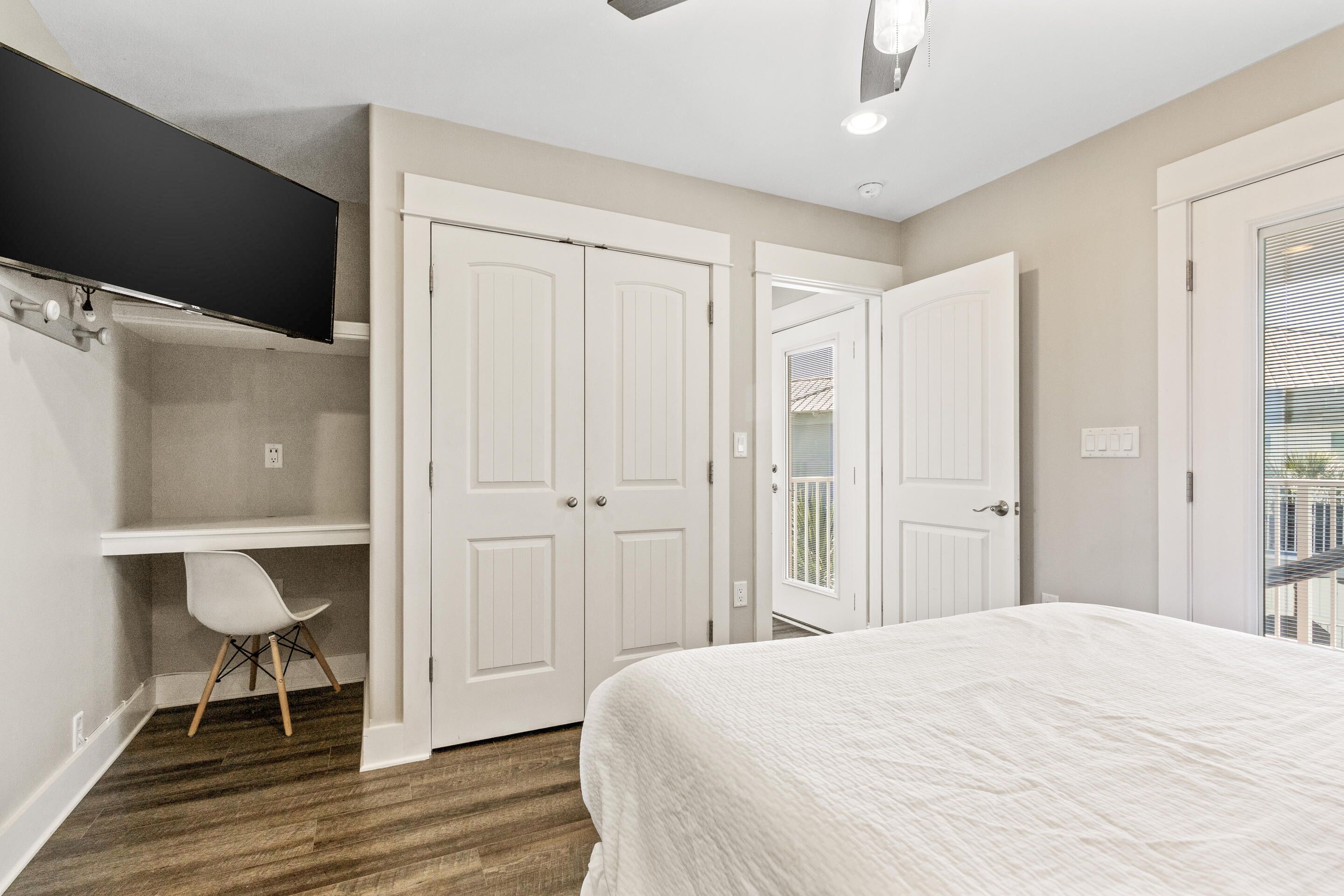 A bedroom with a bed, a desk, and a chair. There are two doors, one of which leads to a balcony.
