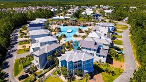 An aerial view of a resort with a central swimming pool, multiple buildings, and surrounding greenery. - Easy Breezy by Southern Vacation Rentals (Santa Rosa Beach)