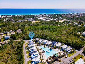 An aerial view of a resort with a central pool, surrounded by villas and a dense forest.