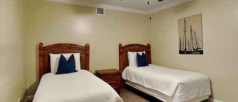 Una habitación de hotel con dos camas individuales, un ventilador de techo, una mesita de noche pequeña y una obra de arte colgada en la pared.