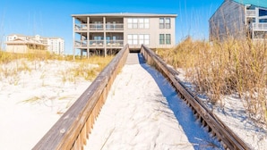 A beachside hotel with a wooden boardwalk leading to a multi-story building with balconies. - Spinnaker #2A by Southern Vacation Rentals (Pensacola)