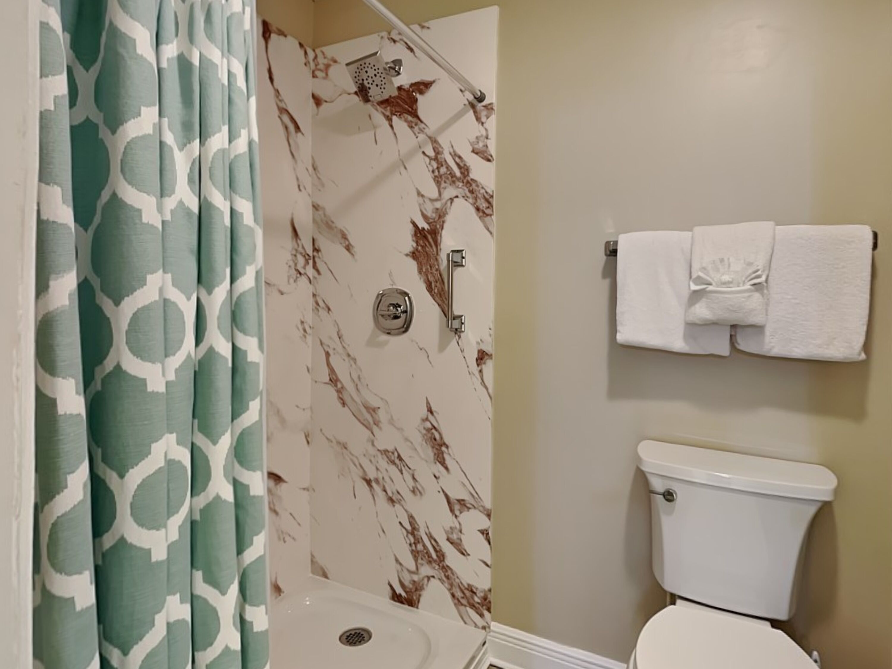 Une salle de bain comprenant des toilettes, une douche avec un mur en marbre et un porte-serviettes avec des serviettes.
