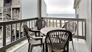 A covered outdoor area with a table and four chairs, overlooking a beach and a building with a staircase. - Spinnaker #2A by Southern Vacation Rentals (Pensacola)