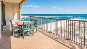Ein Balkon mit Tisch und Stühlen, der Blick auf einen Strand mit klarem, blauem Wasser und sandigem Ufer freigibt.