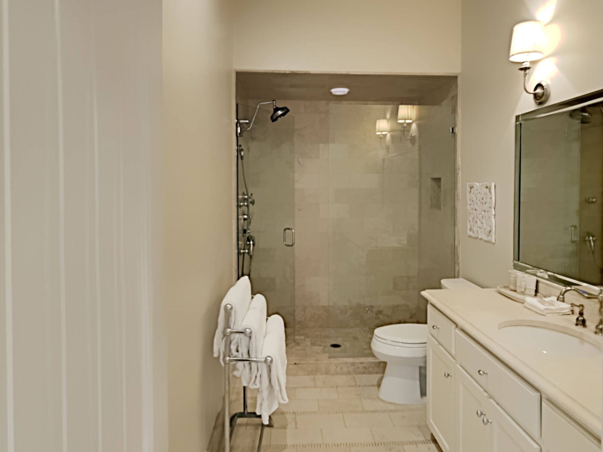 Un baño moderno con cabina de ducha de vidrio, inodoro blanco y tocador con un espejo grande.