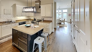 Una cocina moderna con armarios blancos, encimera de granito y una isla central con taburetes.