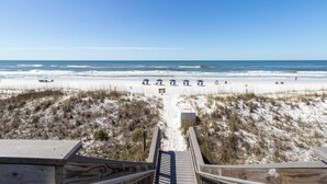 A beach view with a wooden boardwalk leading to the shore, sandy dunes, and the ocean.