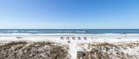 A beach view with a wooden boardwalk leading to the shore, sandy dunes, and the ocean.