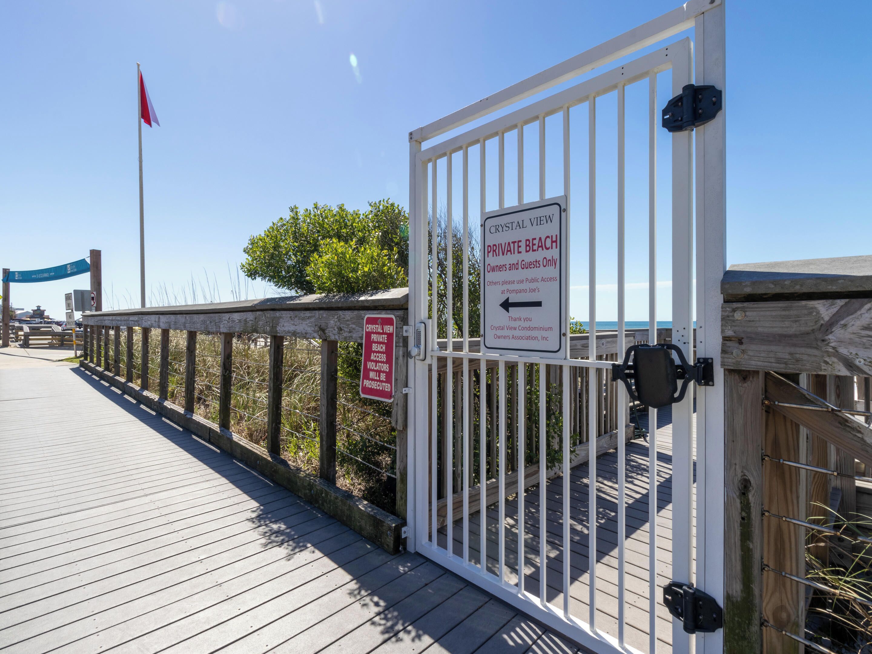 Une promenade en bois mène à une zone délimitée par une barrière, et des panneaux indiquent qu’il s’agit d’une plage privée réservée aux propriétaires et à leurs invités.
