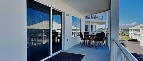 A balcony with a sliding glass door, a small table with chairs, and a view of a building and a parking lot.