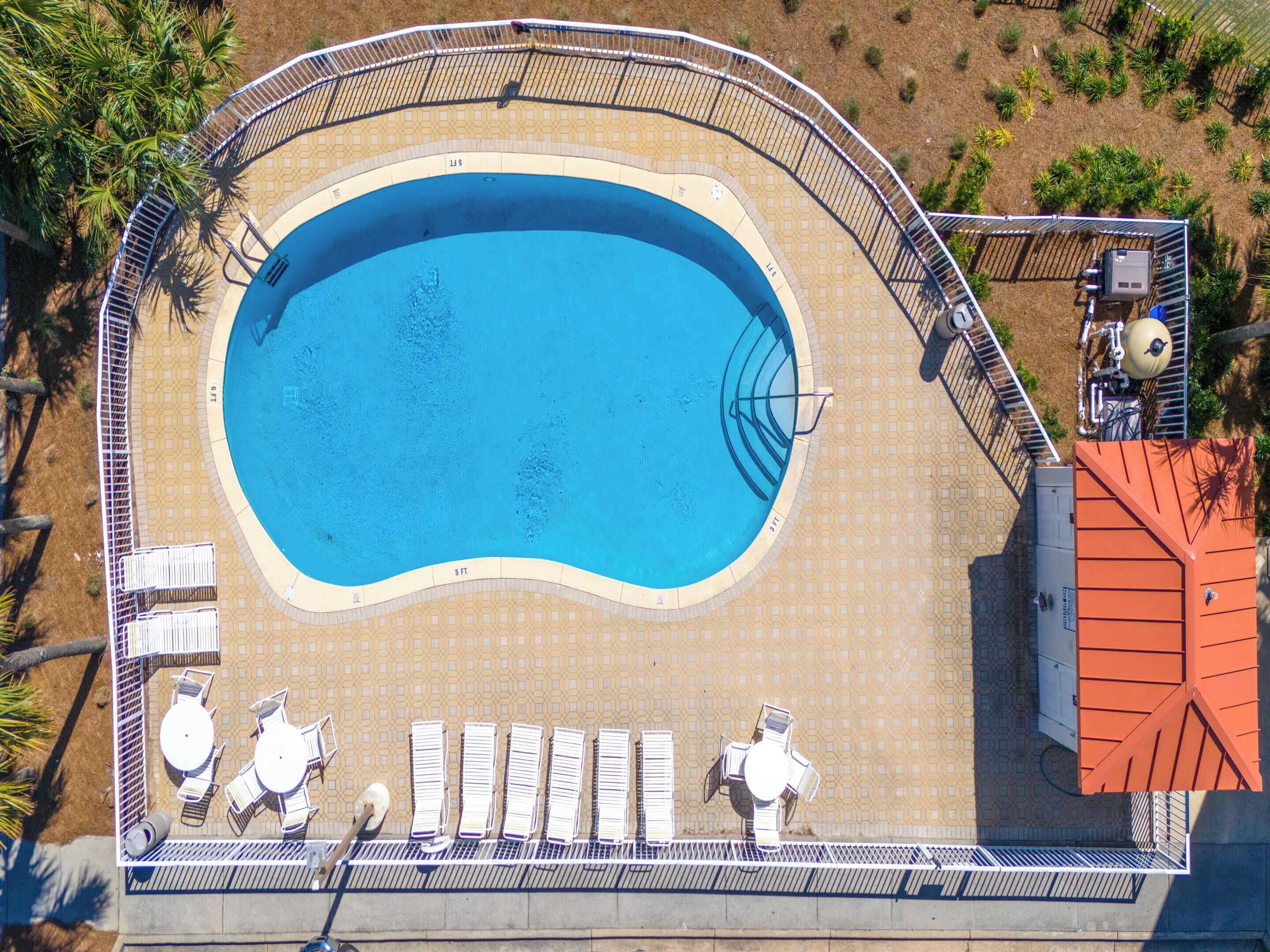 Vue aérienne d’une piscine dotée d’une terrasse carrelée, de chaises longues et d’un espace abrité où se trouve une pompe à eau.