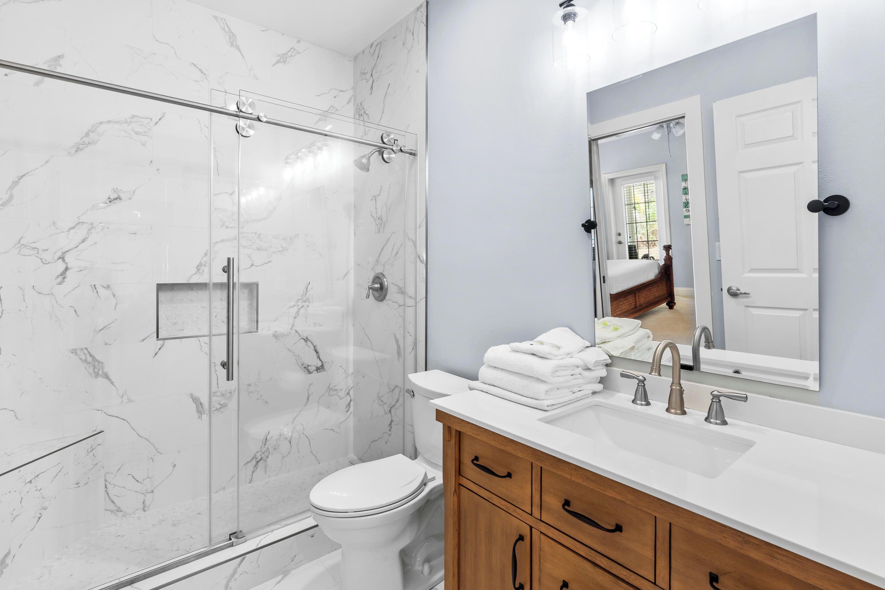 A modern bathroom with a glass-enclosed shower, a white toilet, a wooden vanity with a sink, and a large mirror above the vanity.
