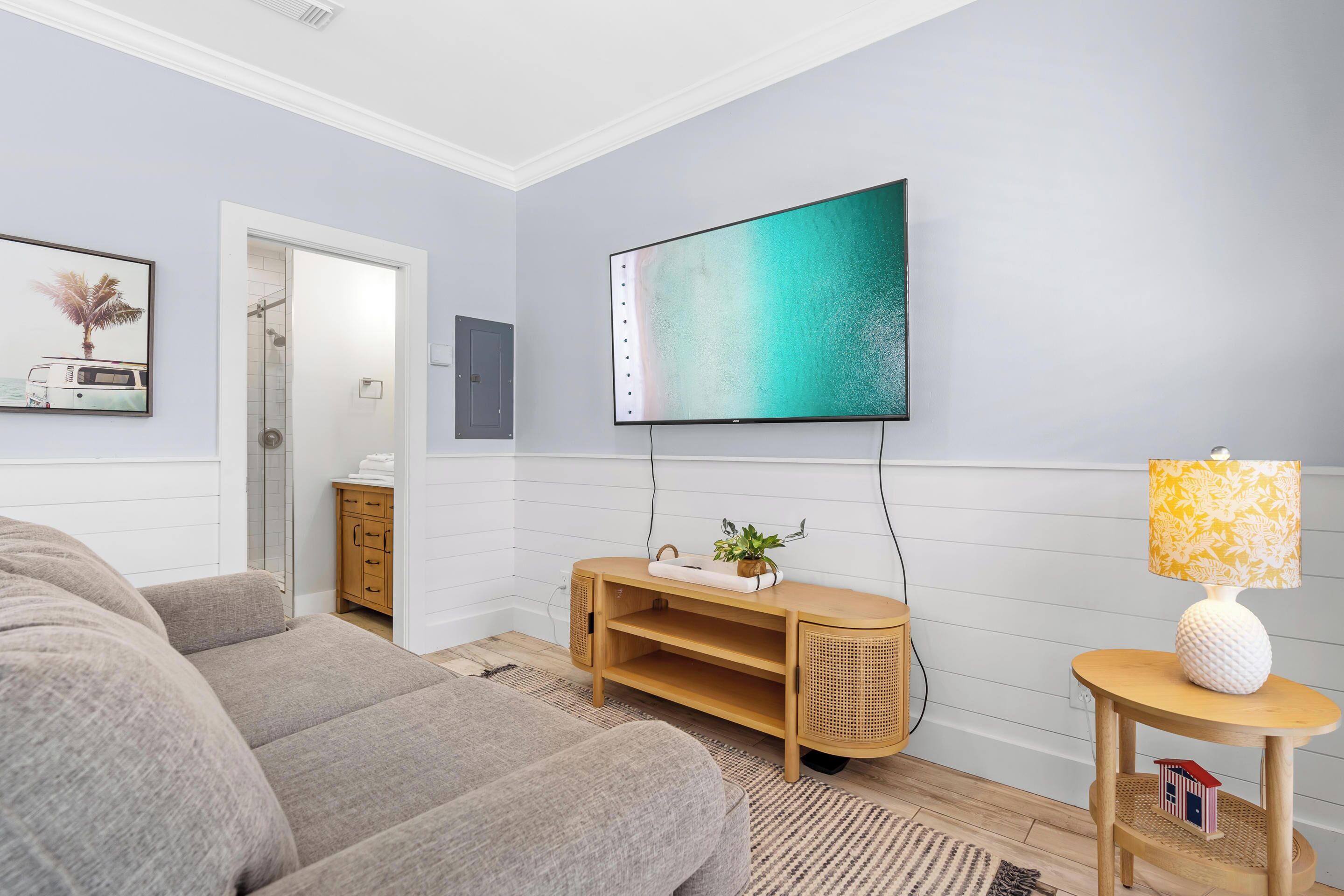A modern living room with a grey sofa, a wooden TV stand with a flat-screen TV, a small lamp, and a framed picture on the wall.