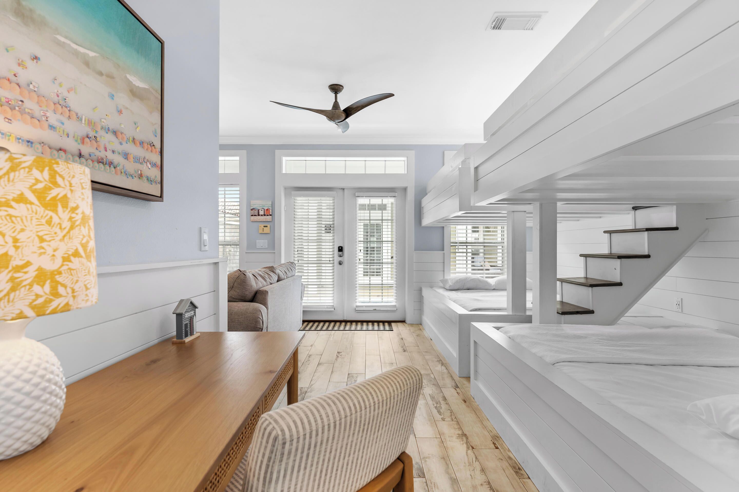 Une chambre moderne avec des lits superposés, une table en bois, un banc et un ventilateur de plafond.