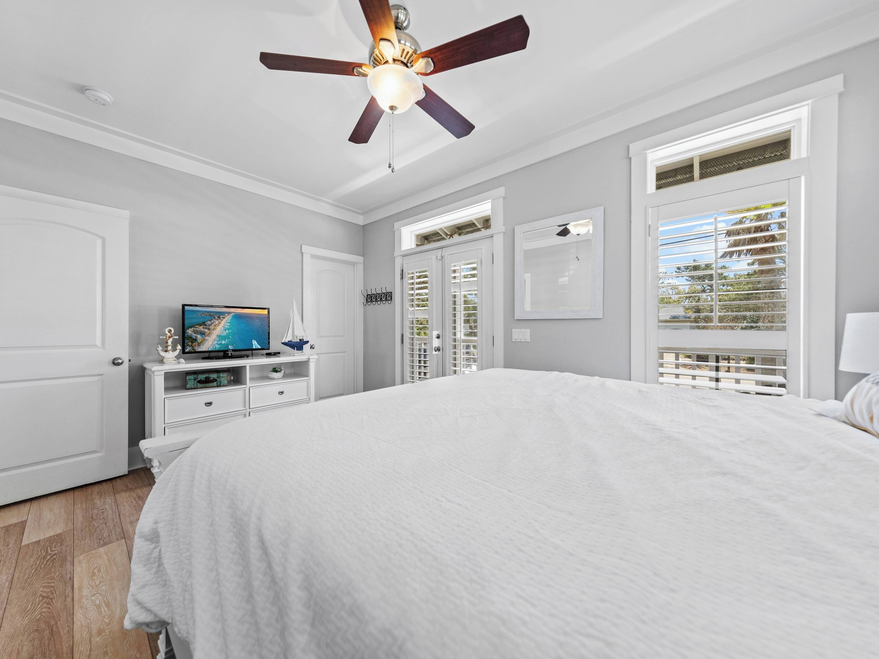 Un dormitorio con una cama grande, un ventilador de techo, un televisor y vistas al exterior a través de la ventana.