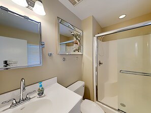 Een badkamer met een wit wastafel, een spiegel, een toilet en een douche met glazen wanden.