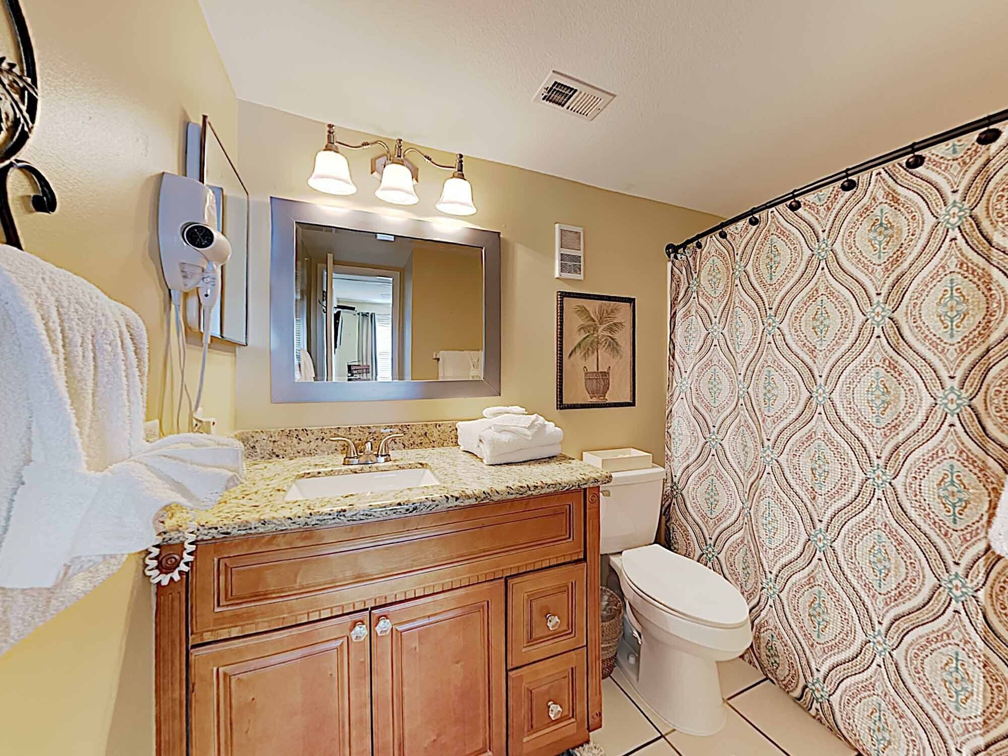 A bathroom with a wooden vanity, a sink, a toilet, and a shower curtain with a patterned design.
