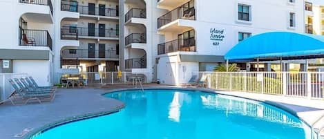 Un hotel de varios pisos con piscina, mobiliario de exterior y una zona cubierta.