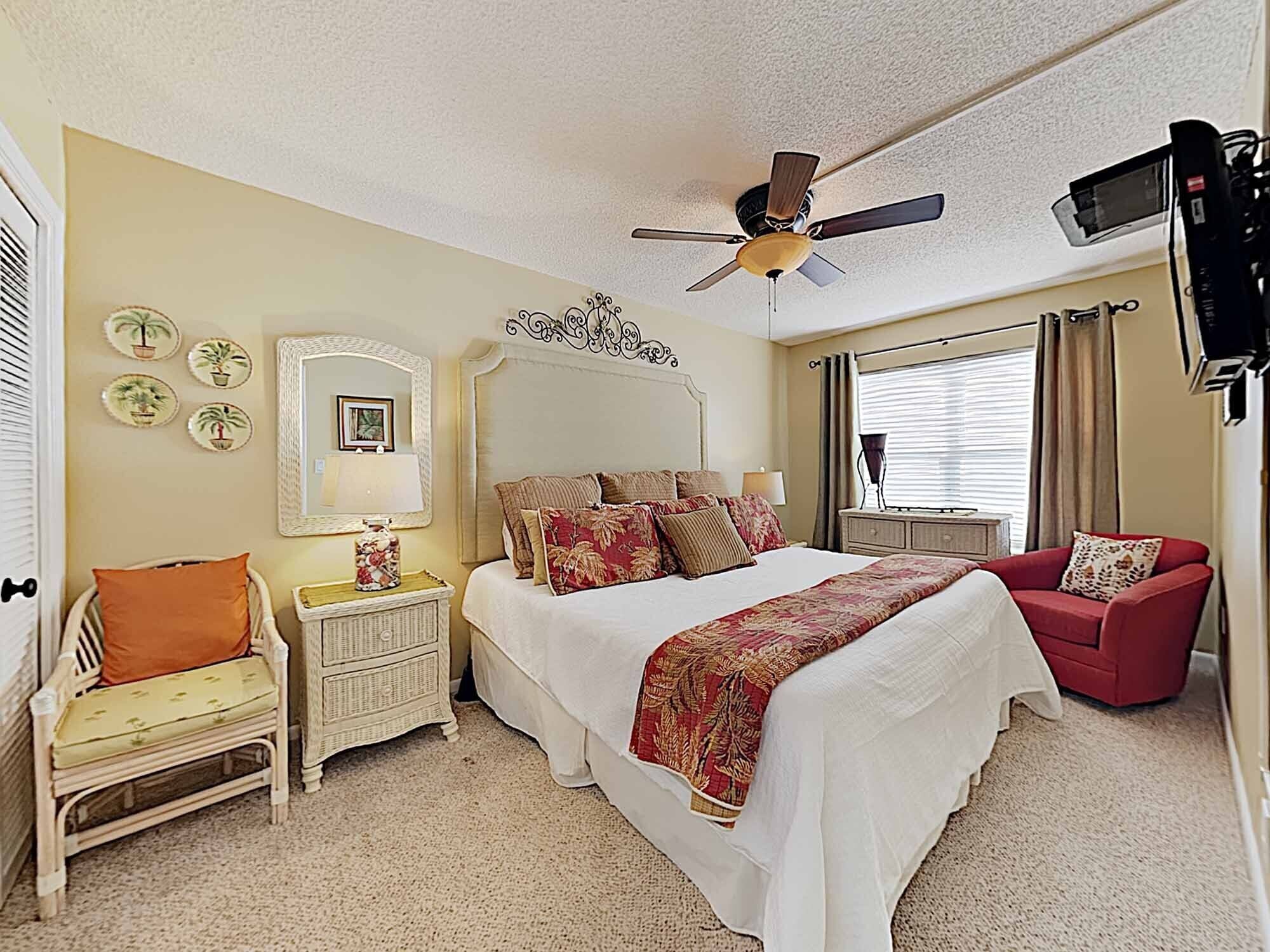 A bedroom with a bed, a nightstand, a chair, a ceiling fan, and a TV.