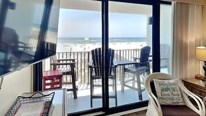 Een balkon met uitzicht op het strand, voorzien van stoelen en een tafel, en een bord met tekst.