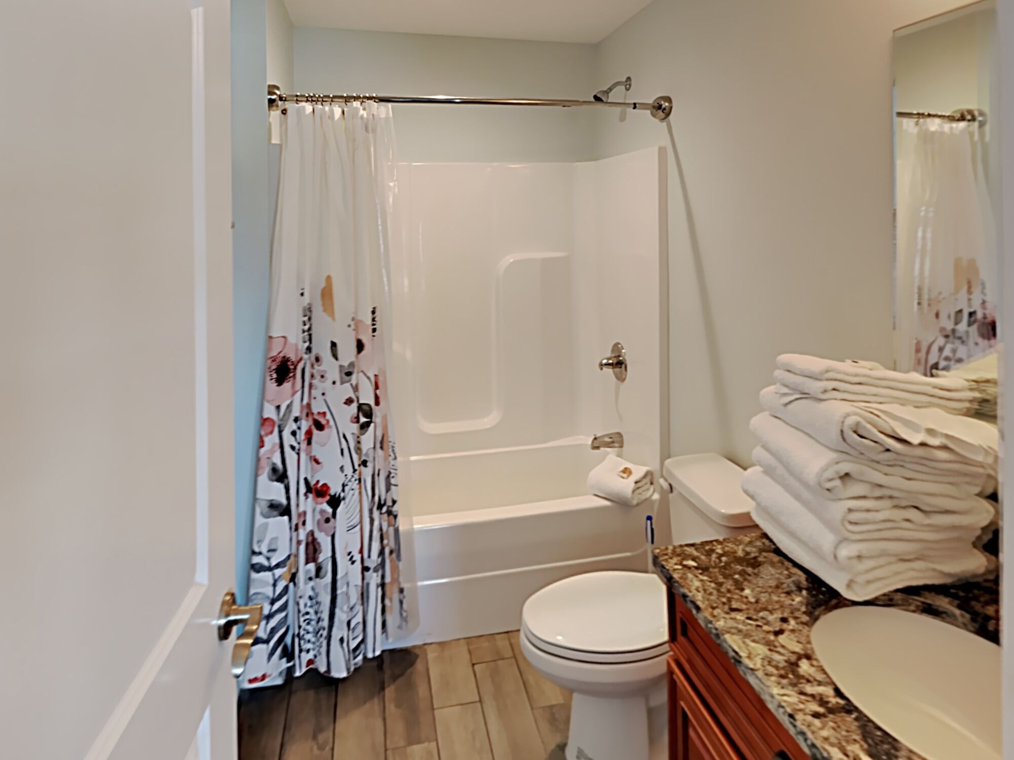 A bathroom with a shower, toilet, and a stack of towels.