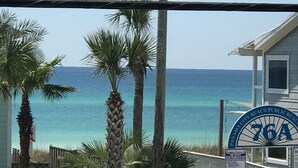 Uma casa na praia com vista para o oceano, palmeiras e uma placa indicando 'Panama City Beach Public Beach'.