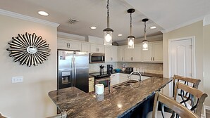 Cozinha com ilha central, eletrodomésticos de aço inoxidável e iluminação pendente.
