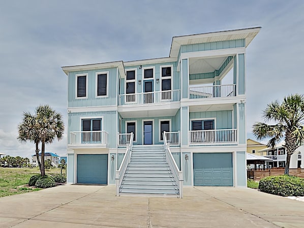 A two-story beachfront house with a central staircase, balconies, and garage doors.
