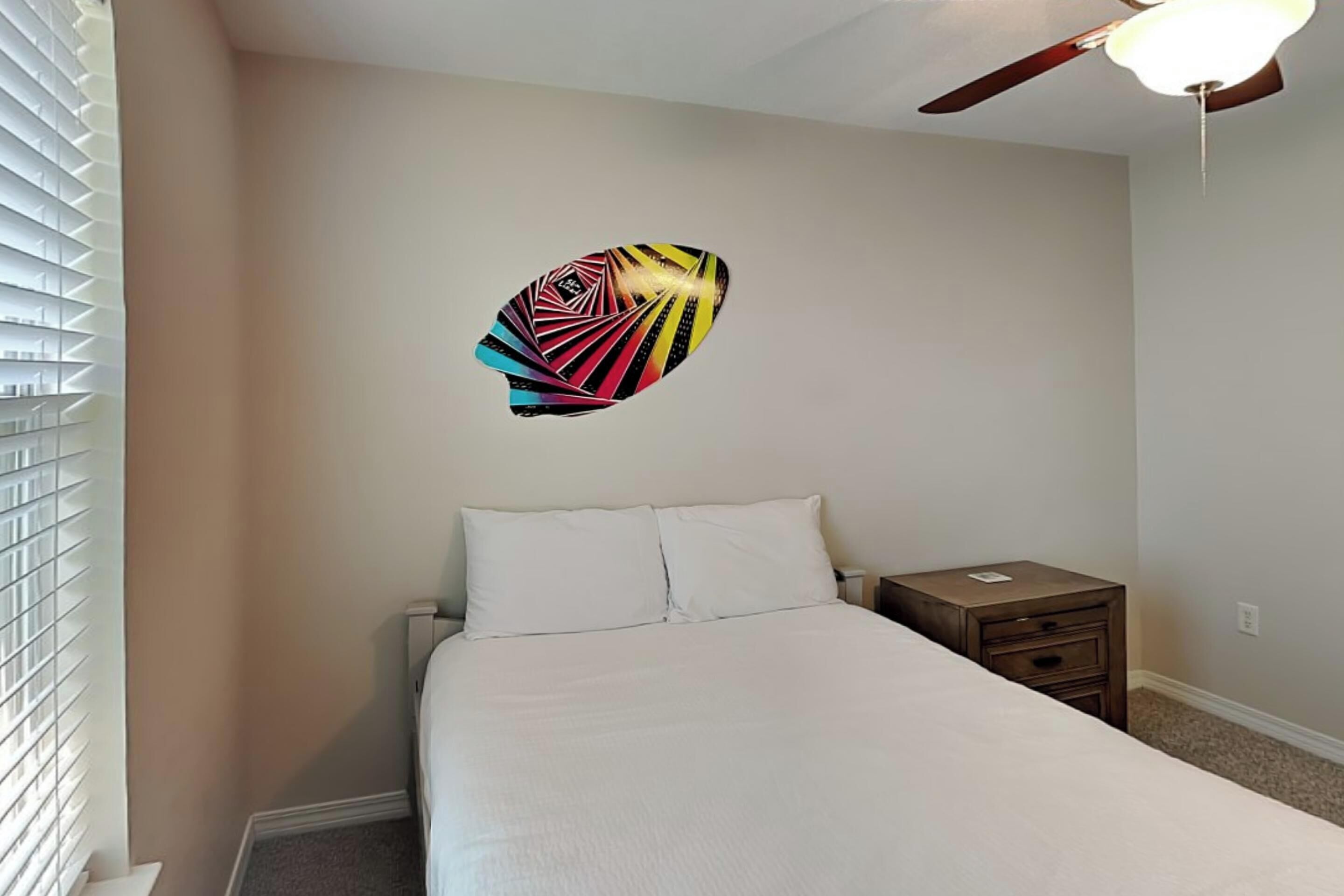 A bedroom with a bed, a nightstand, a ceiling fan, and a wall decoration.
