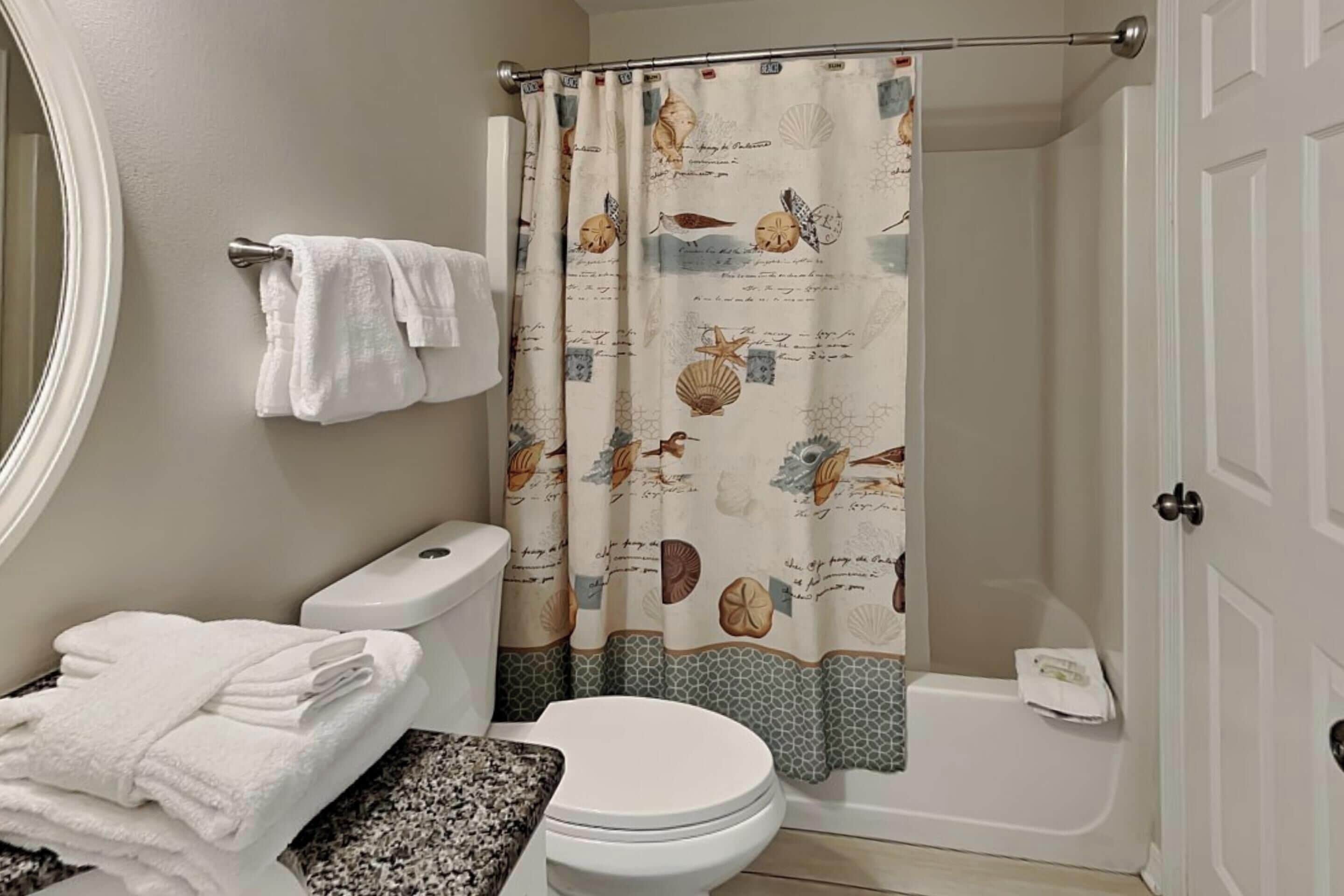 A bathroom with a toilet, sink, and shower curtain with a nautical theme.