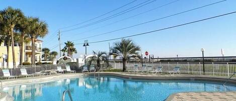 A swimming pool with a tiled deck, surrounded by palm trees and a fence.