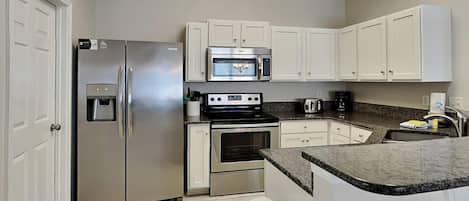 A modern kitchen with white cabinets, stainless steel appliances, a granite countertop, and a built-in oven.