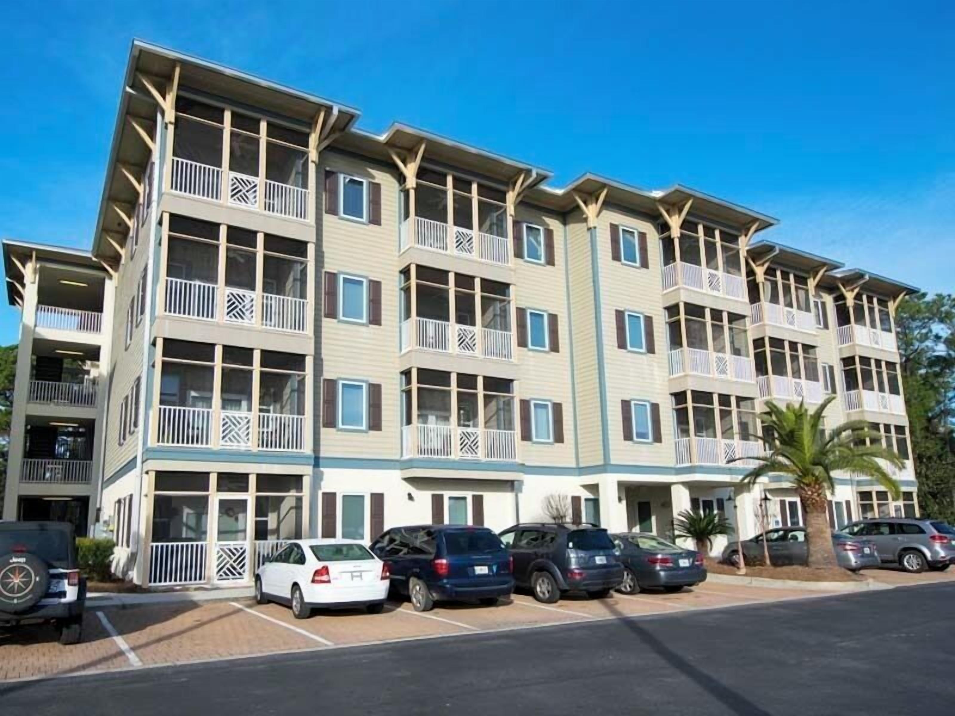 A multi-story hotel with balconies, a parking lot, and a palm tree.
