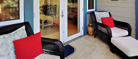 A covered patio area with wicker furniture and a sliding glass door leading to an outdoor deck.