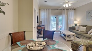 A modern living room with a glass dining table, a sofa, and a ceiling fan. - Seagrove Highlands by Southern Vacation Rentals (Santa Rosa Beach)